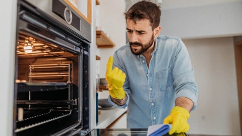 Een man met gele schoonmaakhandschoenen maakt zijn oven schoon.